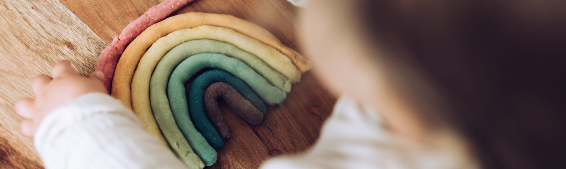 Kleinkind knetet bunten Regenbogen auf Holztisch